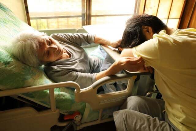 介護疲れで要介護者のベットにもたれて寝ている介護者